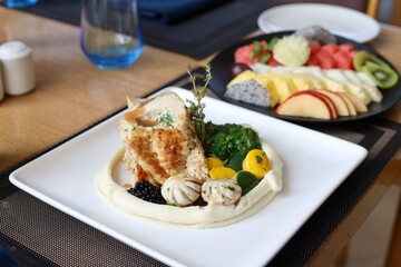 Grilled chicken with vegetables on the side served on a fancy white plate in a restaurant or cafe background 