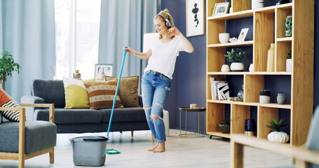 Girl, cleaning and singing with headphones in home, broom and happy with streaming in living room....