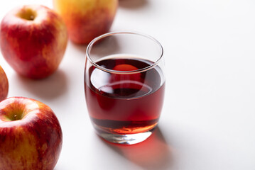 Glass of apple cider with red apple fruit on white background