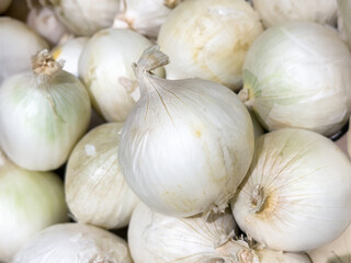 Fresh white onions close-up, piled together in a box, natural texture of bulbs, ideal for cooking, healthy eating, grocery sale, and vegetable background.
