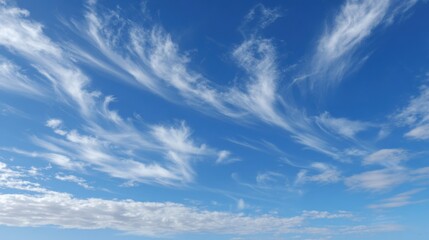 Fototapeta premium Wispy white clouds swirl gently against a vibrant blue sky, creating a serene atmosphere during a sunny afternoon near the coast, perfect for relaxation and reflection.