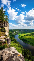 Obraz premium High-angle view of a river winding through a valley, with dramatic sandstone cliffs in the foreground and lush green landscape. Vast blue sky with scattered white clouds