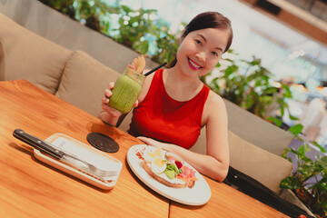 A smiling young woman enjoys a healthy, fresh salmon sandwich for a nutritious meal at Bartels Thailand at True Digital Park in Bangkok