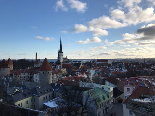 Obraz premium Scenic panoramic view of Tallinn Old Town from Kohtuotsa viewing platform. Red rooftops, medieval towers, and St. Olaf’s Church spire rise against the Baltic Sea horizon under a bright winter sky.