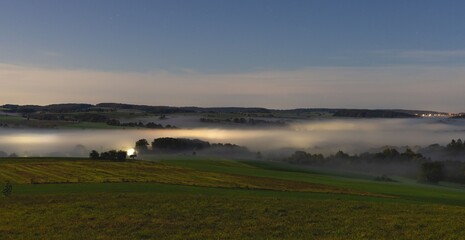 Misty valley at dusk with rolling hills.
