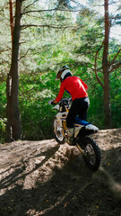 Naklejka premium A enduro man jumps a dirt bike in a forest, from the back