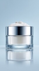 Obraz premium A clear glass jar with a silver lid holds a thick, off-white cream; a swirl of cream peaks above the rim, reflecting light against a pale blue background