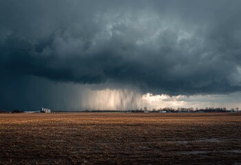 Dramatic storm clouds over a field.  Rain pouring down.  Vast, dark, ominous clouds.  Golden, dry, muddy field below