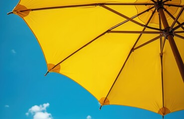 Bright yellow umbrella stands against vivid blue sky, offering shade on a sunny summer beach day in Thailand. Vacation, relaxation, and tropical holiday vibes emanate from this tranquil seaside scene.
