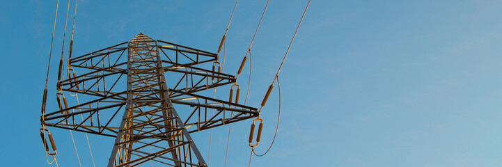 Low-angle view of a steel lattice tower supporting high-voltage lines. The warm sunlight contrasts with the cool sky, representing energy, technology, and industrial design.
