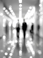 Blurred grayscale image shows three figures walking down a corridor with rows of lights creating a bokeh effect. The focus is soft and ethereal