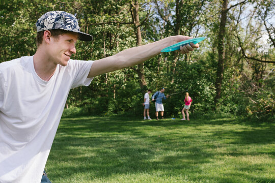 Teen boy prepares to throw disc golfing disc with family playing