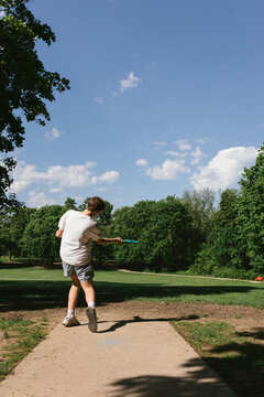Teen releases disc golf frisbee towards forest over field in sunshine