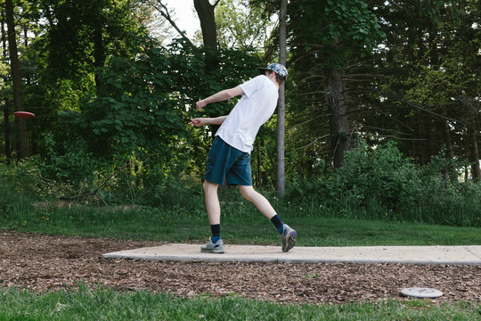 Teenage boy throws driver off disc golf tee box in forest
