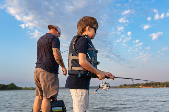 Boy fishing with man on boat wearing lifejackets on lake