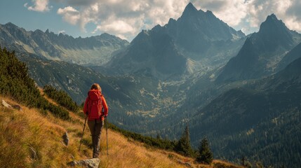 Fototapeta premium A lone hiker wearing a bright jacket walks along a rocky path in the mountains, surrounded by stunning peaks and lush greenery at sunset. The sky glows with warm colors.