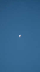 Minimalist photo of a half moon in a clear blue sky, symbolizing calmness and simplicity.