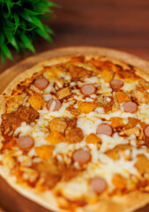 Close up tasty chicken sausage crispy thin pizza baked on wooden plate, delicious melting mozzarella cheese on wooden board, homemade cooking ingredients lying on dark background, food advertisement.