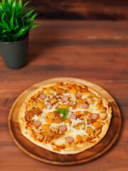 Tasty chicken and sausage crispy pizza flatbread baked on wooden plate, delicious melting mozzarella cheese on wooden board, homemade cooking ingredients lying on dark background, food advertisement.