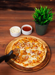 Tasty chicken and sausage crispy pizza on wooden plate using pizza cutter to slice delicious melting mozzarella cheese on board homemade cooking ingredient lying on dark background, food advertisement