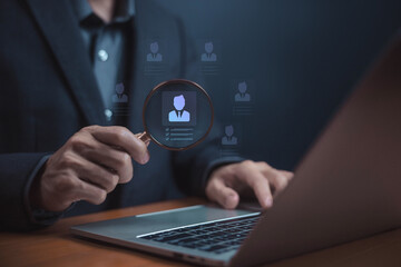 Recruitment and HR technology concept. A businessman using a magnifying glass to review a candidate profile on laptop, symbolizing hiring process, employee evaluation, and talent acquisition strategy.