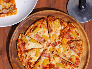 Top view pineapple and ham hawaiian pizza and chicken and sausage pizza on wooden plate, delicious melting cheese on wooden board, homemade cooking ingredients on dark background, food advertisement.