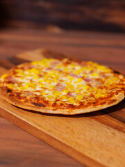 Tasty corn and bacon crispy pizza flatbread baked on baking steel plate, delicious melting mozzarella cheese on wooden table, homemade cooking ingredients lying on dark background, food advertisement.