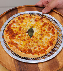 Tasty cheese crispy pizza flatbread baked on baking steel plate, delicious melting mozzarella cheese on wooden table board, homemade cooking ingredients lying on dark background, food advertisement.