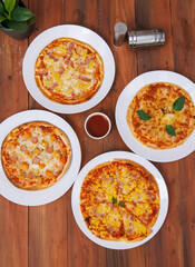 Top view of composition different delicious tasty crispy pizza, flatbread baked on white dish with decoration on wooden table, homemade cooking ingredients lying on dark background, food advertisement