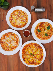 Top view of composition different delicious tasty crispy pizza, flatbread baked on white dish with decoration on wooden table, homemade cooking ingredients lying on dark background, food advertisement