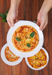 Top view of composition different delicious tasty crispy pizza, flatbread baked on white dish with decoration on wooden table, homemade cooking ingredients lying on dark background, food advertisement