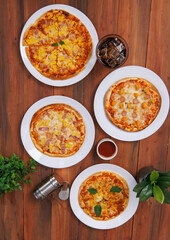 Top view of composition different delicious tasty crispy pizza, flatbread baked on white dish with decoration on wooden table, homemade cooking ingredients lying on dark background, food advertisement