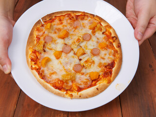 Tasty pineapple and ham hawaiian pizza baked on baking steel plate, delicious melting mozzarella cheese on wooden board, homemade cooking ingredients lying on dark background, food advertisement.