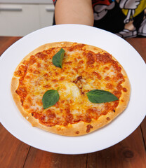 Tasty cheese crispy pizza flatbread baked on white dish plate, delicious melting mozzarella cheese on wooden table board, homemade cooking ingredients lying on dark background, food advertisement.