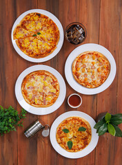 Top view of composition different delicious tasty crispy pizza, flatbread baked on white dish with decoration on wooden table, homemade cooking ingredients lying on dark background, food advertisement