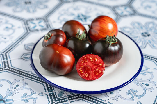 Ripe red and black beauty tomatoes on white plate with blue rim. Tiled kitchen table. Cooking with copy space. Tomatocore