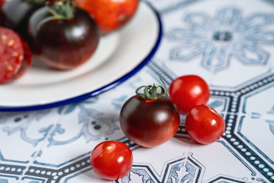 Ripe red and black beauty tomatoes on white plate with blue rim. Tiled kitchen table. Cooking with copy space