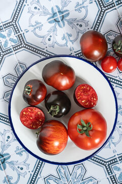 Ripe red and black beauty tomatoes on white plate with blue rim. Tiled kitchen table. Cooking with copy space