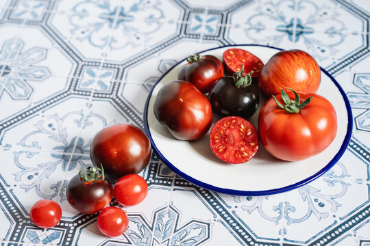 Ripe red and black beauty tomatoes on white plate with blue rim. Tiled kitchen table. Cooking with copy space. Tomatocore