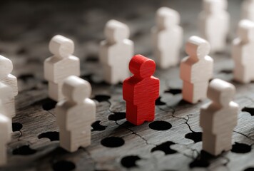 A red wooden figure stands out amidst a crowd of white figures on a cracked, textured wooden surface with dark, round holes