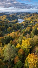 An aerial view of an autumn landscape featuring lush forests in warm colors, rolling hills, and a tranquil lake under a sky streaked with clouds
