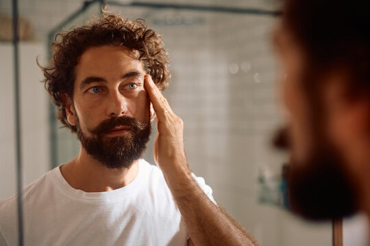 Mature man looking at himself in mirror in bathroom.