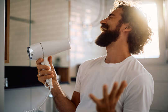 Playful man having fun while blow drying his hair in bathroom.