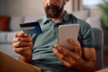 Close up of man mbanking with credit card and cell phone at home.