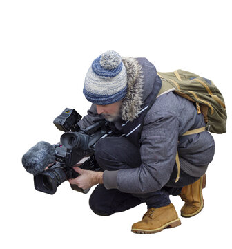 cam&eacute;raman accroupi, portant une veste chaude et un bonnet, filmant avec une cam&eacute;ra professionnelle, sac &agrave; dos kaki, chaussures de randonn&eacute;e, p&eacute;riode hivernale