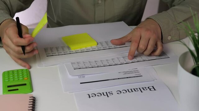 A professionals hands cross-reference figures between a calculator and printed financial statements, then annotate and label the documents for clarity. This clip is perfect for content about auditing