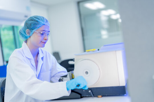 Scientist conducts analysis in laboratory adjusting equipment while wearing protective gear and focused expression