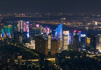 Fototapeta premium Distant cityscape view of lit skyscrapers and buildings in Hangzhou, China at night with illuminated river in the background
