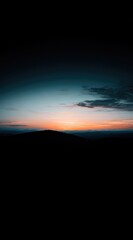 Striking horizon view A dark mountain silhouette against a vibrant, colorful gradient sky at sunset/sunrise, with a few clouds