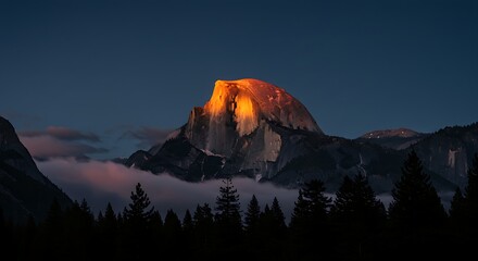 Half dome peak illuminated by the setting sun, with clouds and silhouetted trees in yosemite national park